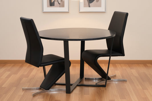 A modern round dining table with a black top and black metal base, accompanied by two black upholstered chairs with sculptural chrome legs.